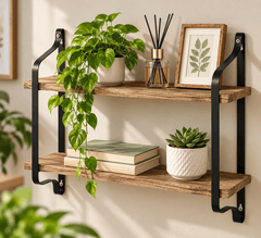 Two tier wall shelf with rustic wood boards and black metal brackets holding a plant, a framed print, books and a diffuser