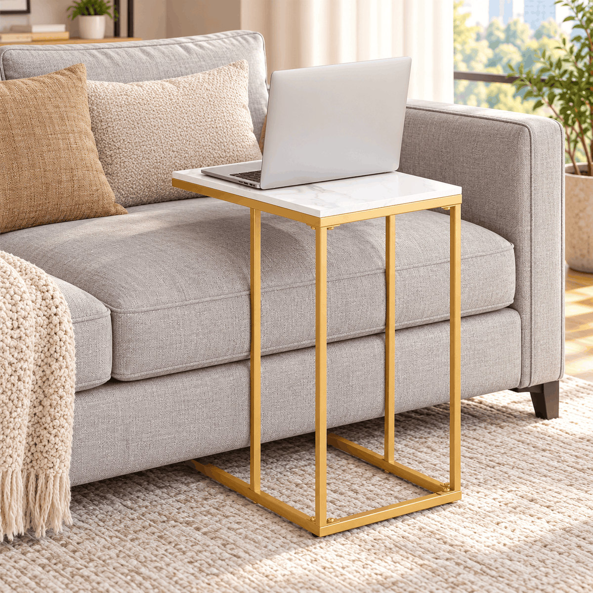 Gold frame C shaped table with a white top holding a laptop next to a grey sofa in a bright living room