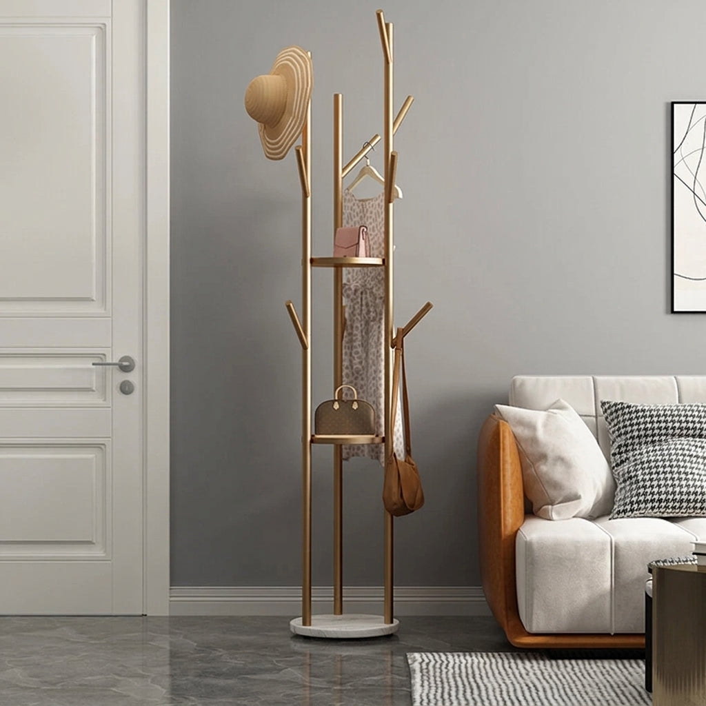 Gold tree coat rack with a hat, dress on a hanger and shoulder bag on the branches and handbags on the two round shelves