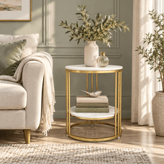 Round two tier side table with a gold frame and marble look tops beside a sofa holding olive stems, a small vase and books