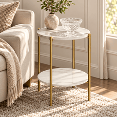 White marble look round side table with gold legs beside a sofa holding a vase with leaves and a glass bowl on the top